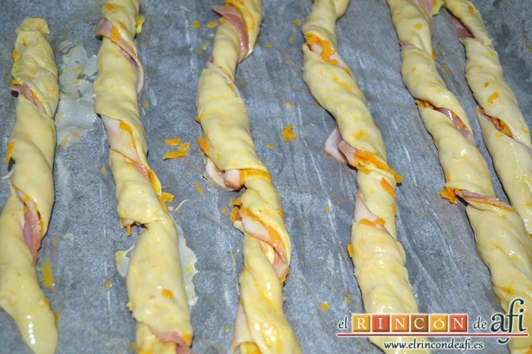 Rizos de bacon y queso cheddar curado de Lorraine Pascale, cortar las tiras y enrollarlas sobre el papel de horno