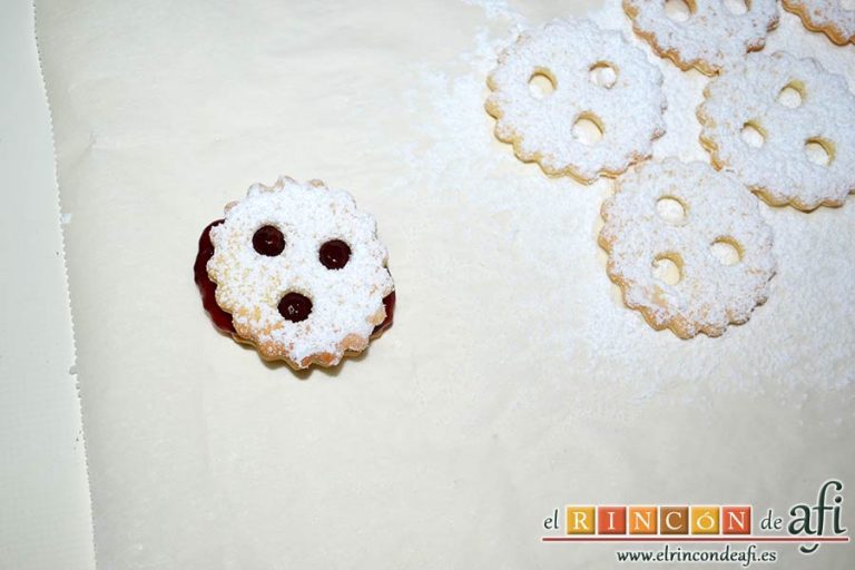 Galletas con masa quebrada y mermelada de frambuesas, cubrirla con una de las galletas agujereadas y cubiertas de azúcar glass