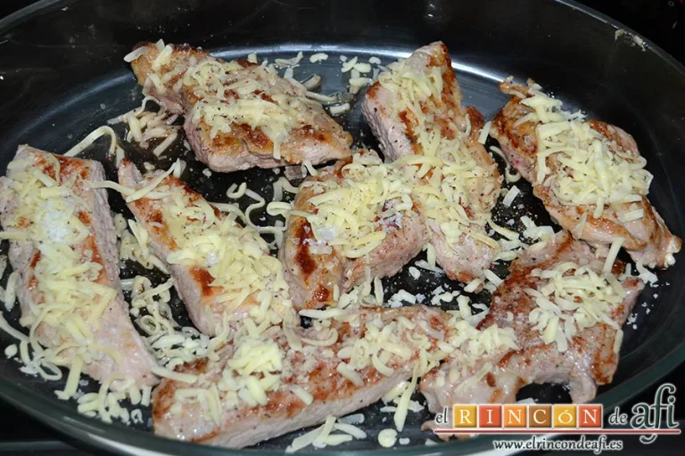 Secreto de cerdo al horno con papas panaderas y pimiento rojo, ponerlos en una bandeja, espolvorear pimienta, sal y queso rallado